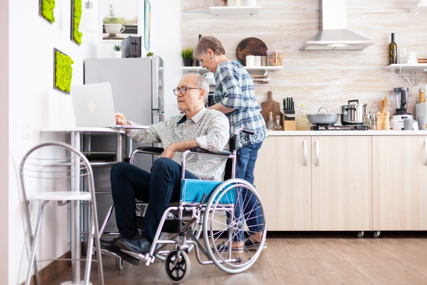 elderly man in a wheelchair typing on a laptop in a kitchen